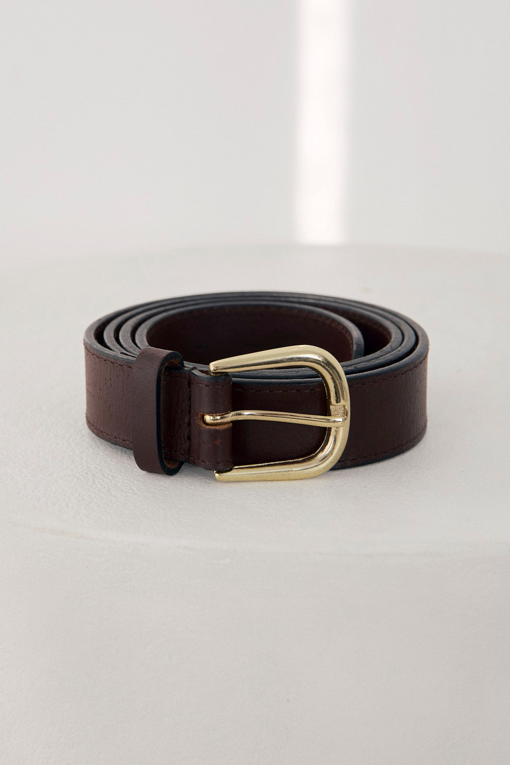 Black leather belt with a gold buckle on a light gray background