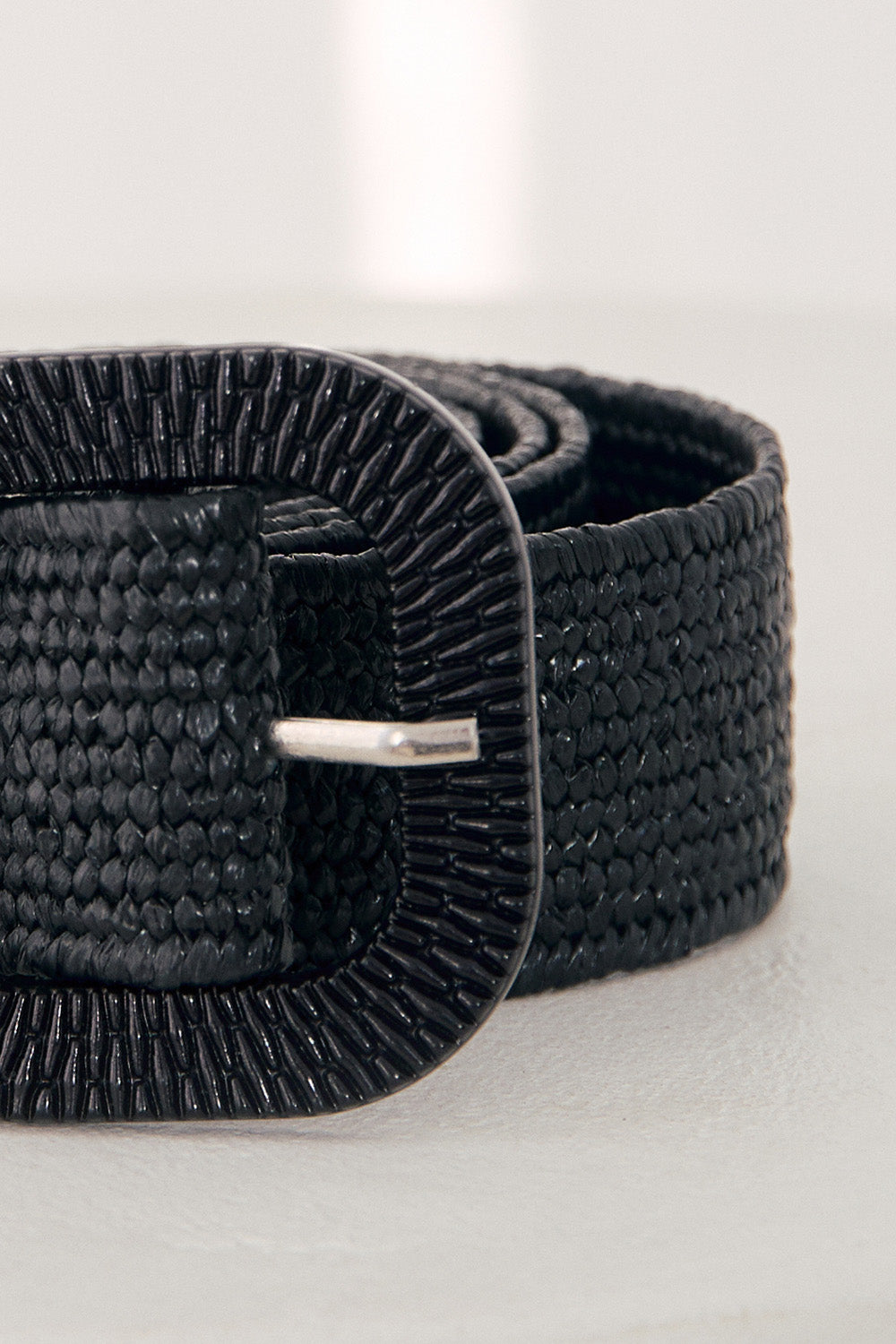 Black woven belt with a silver buckle on a light gray background