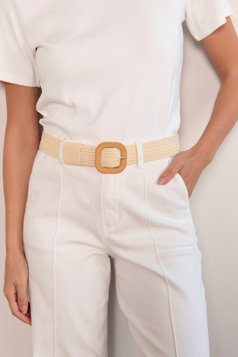 Person wearing a white outfit with a beige belt and pants on a plain background