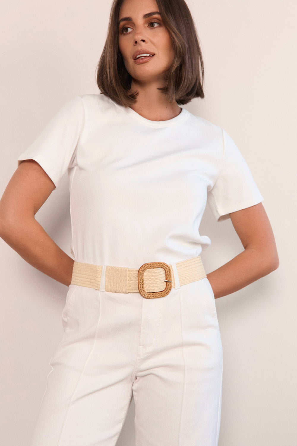 Woman wearing a white outfit with a beige belt against a plain background