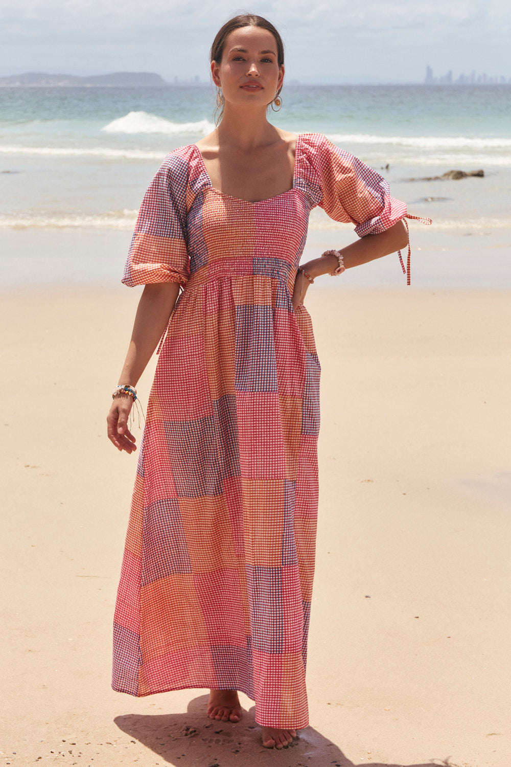 Woman in a checkered dress standing on a beach with ocean in the background