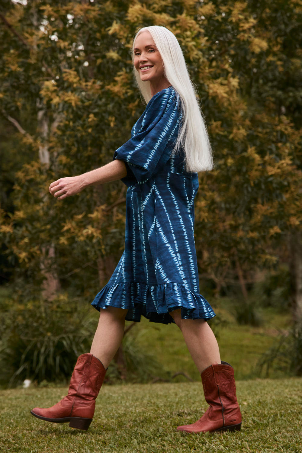 Woman in a blue dress and red boots standing outdoors with trees in the background
