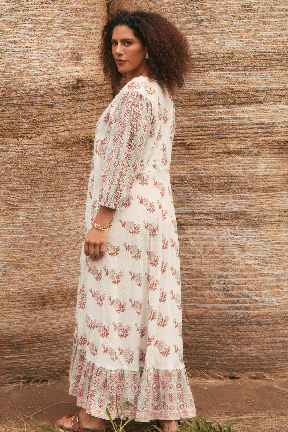 Woman wearing a white floral dress against a textured wall.