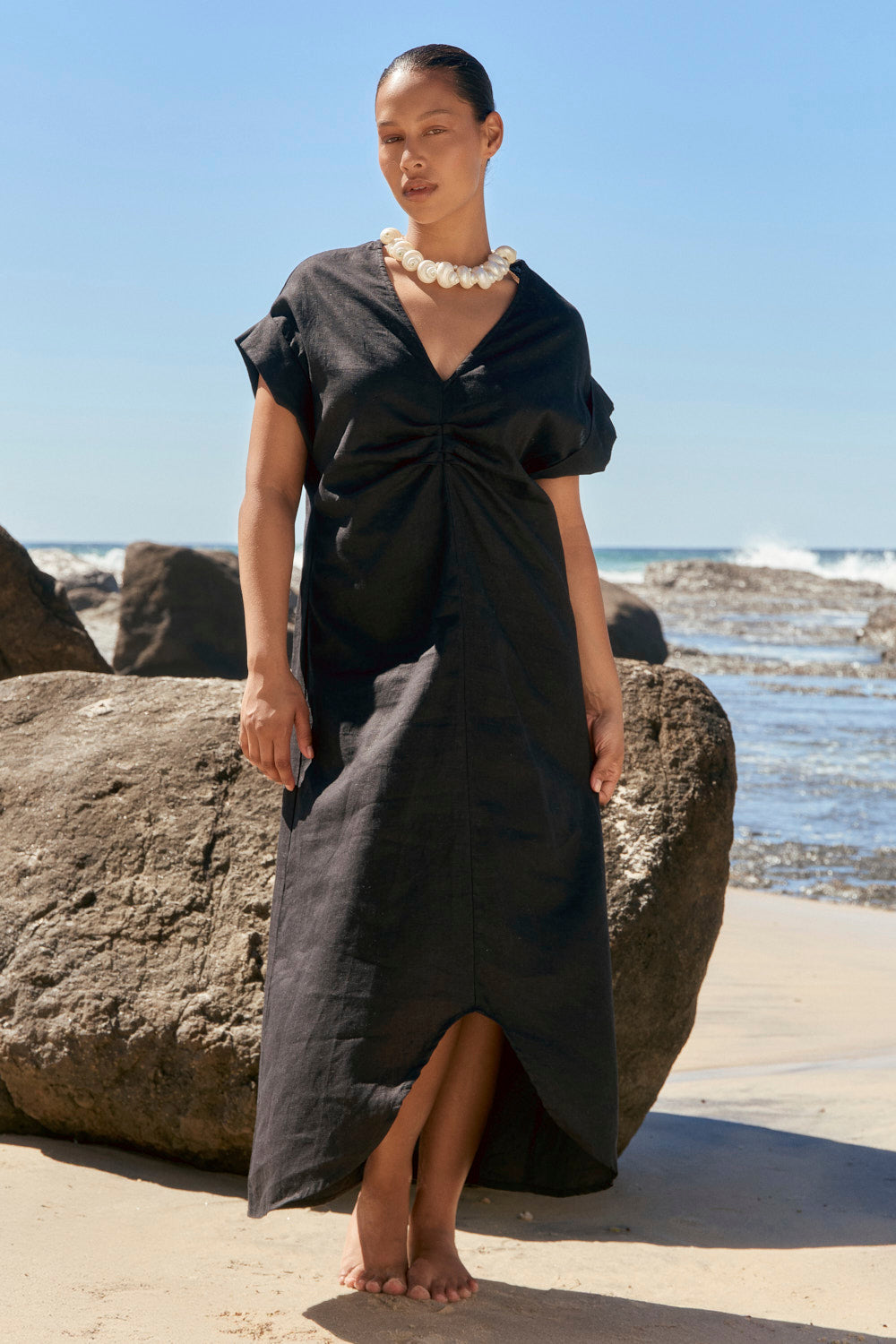 Woman in a black dress standing on a beach with ocean and sky in the background