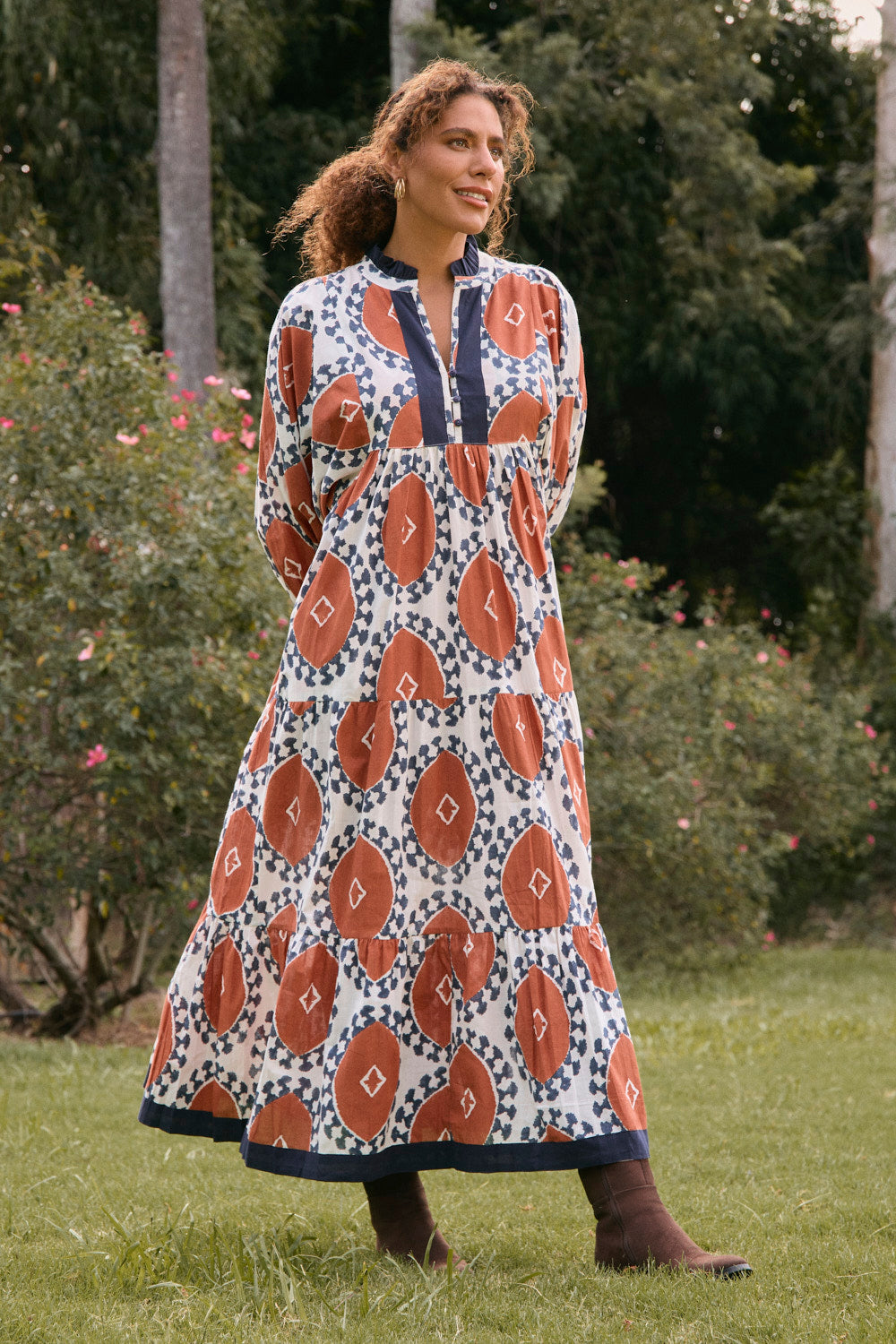 Woman wearing a patterned dress standing outdoors with greenery in the background