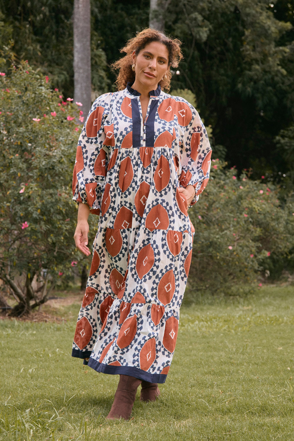 Woman wearing a patterned dress standing in a grassy area with trees in the background