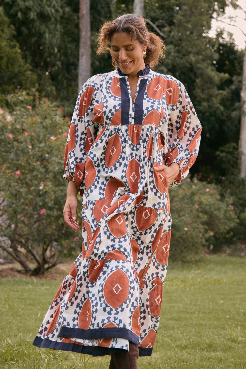 Woman wearing a patterned dress standing outdoors with greenery in the background