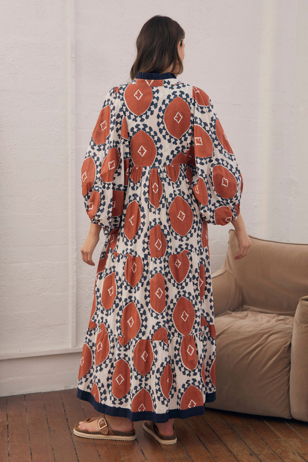 Woman wearing a patterned dress standing in a room with a couch.