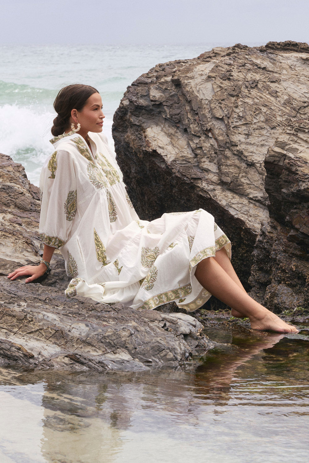 Woman in a white dress sitting on rocks by the water