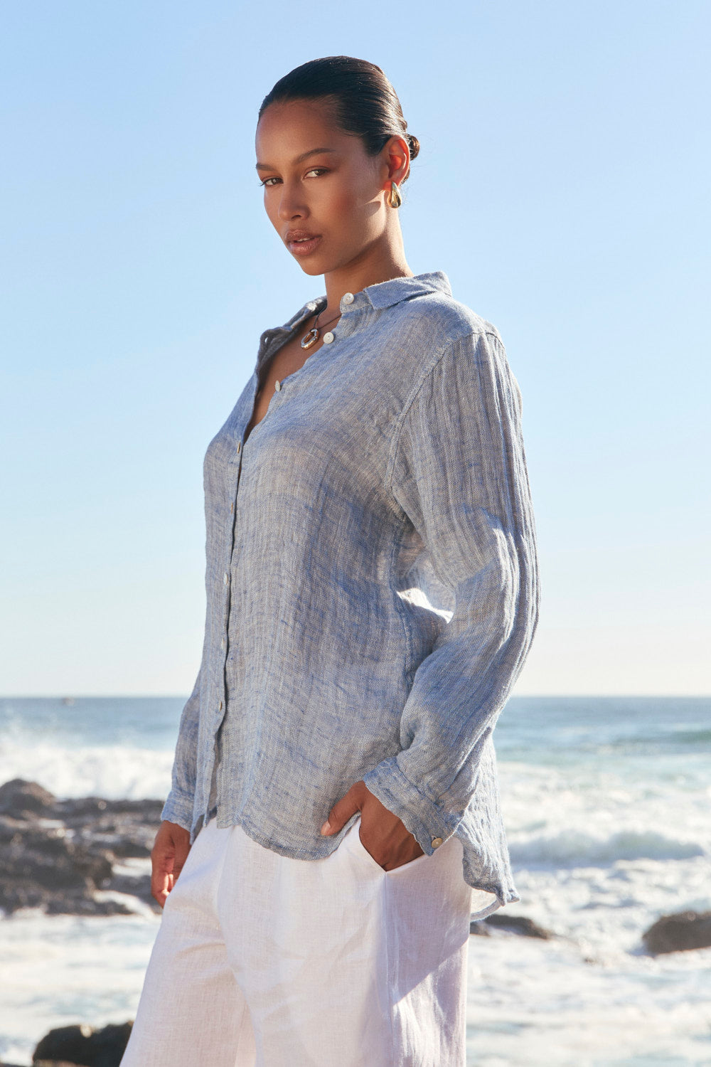 Woman wearing a light blue shirt and white pants standing on a beach.