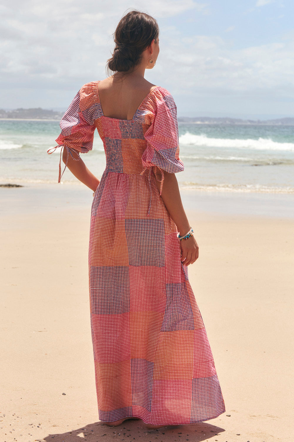 Woman in a colorful dress standing on a beach with ocean waves in the background