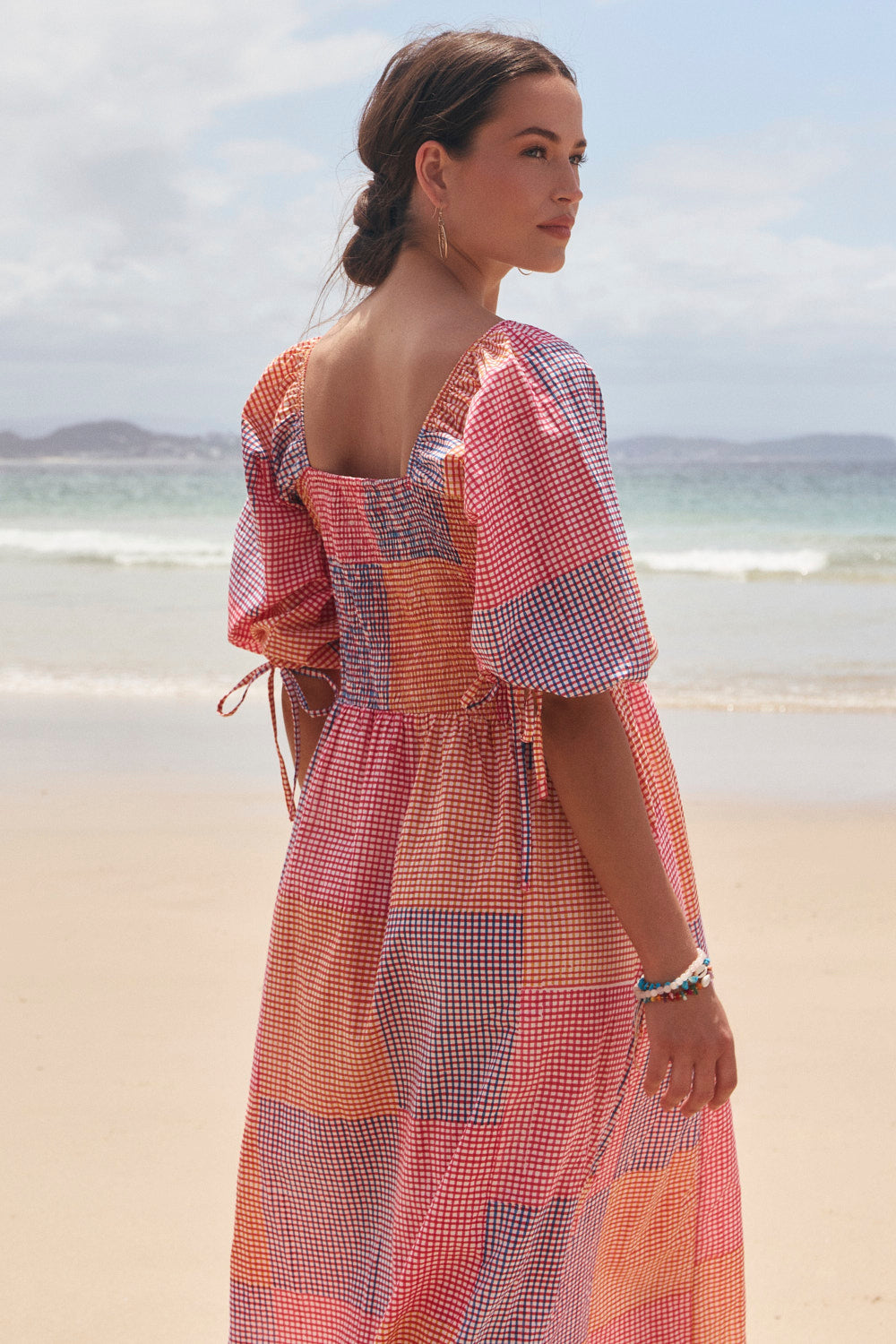 Woman in a colorful dress standing on a beach with ocean and sky in the background