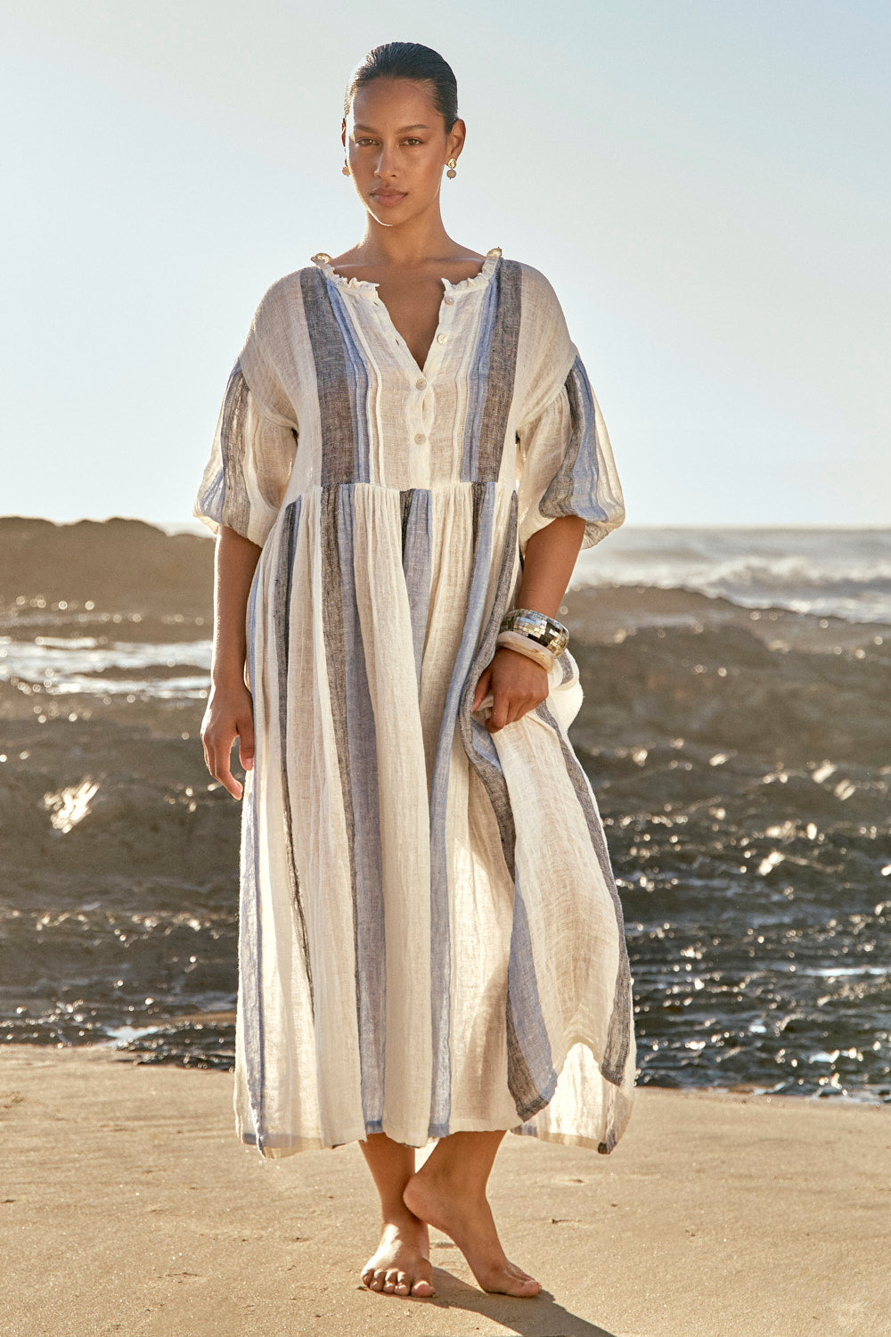 Woman in a striped dress standing on a beach with ocean in the background