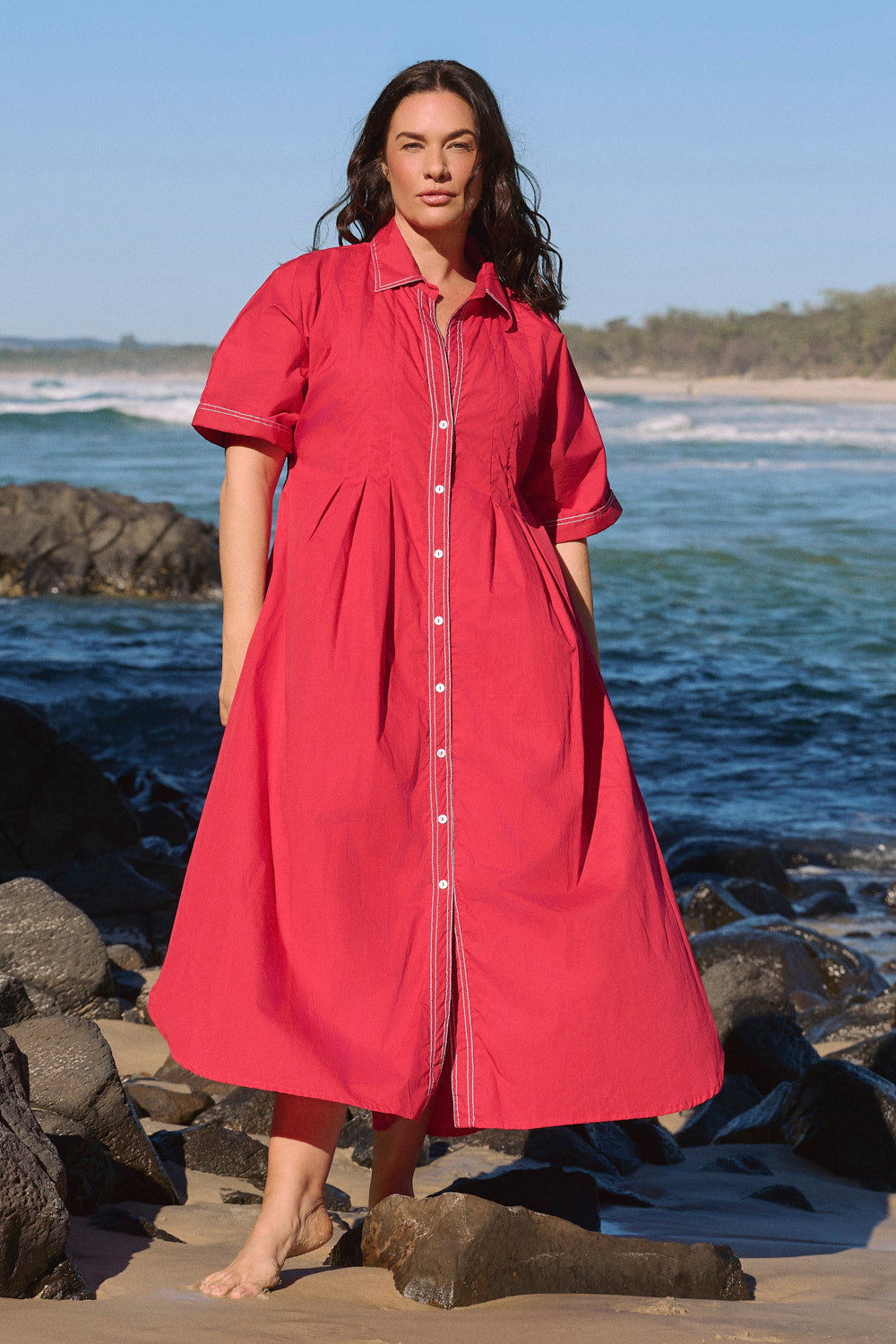 Model wearing the Bridget Pleated Dress in Red Poplin with short rolled-cuff sleeves and pockets, Adrift Clothing
