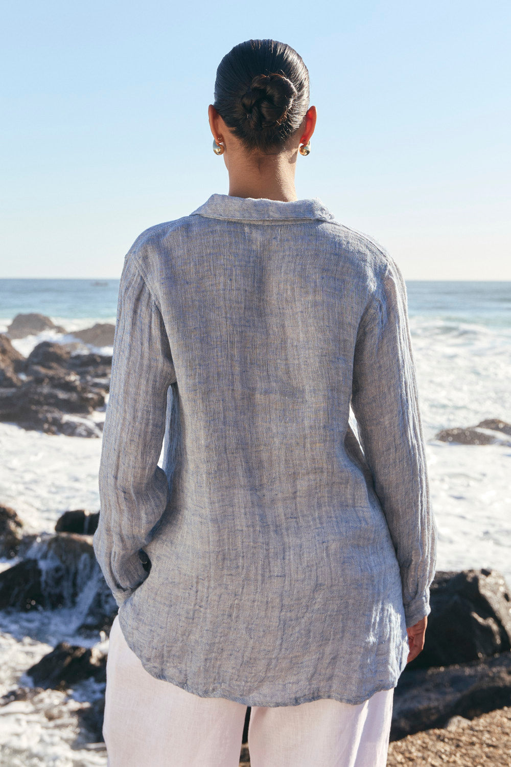 Person wearing a light gray textured shirt standing on a rocky beach with ocean view