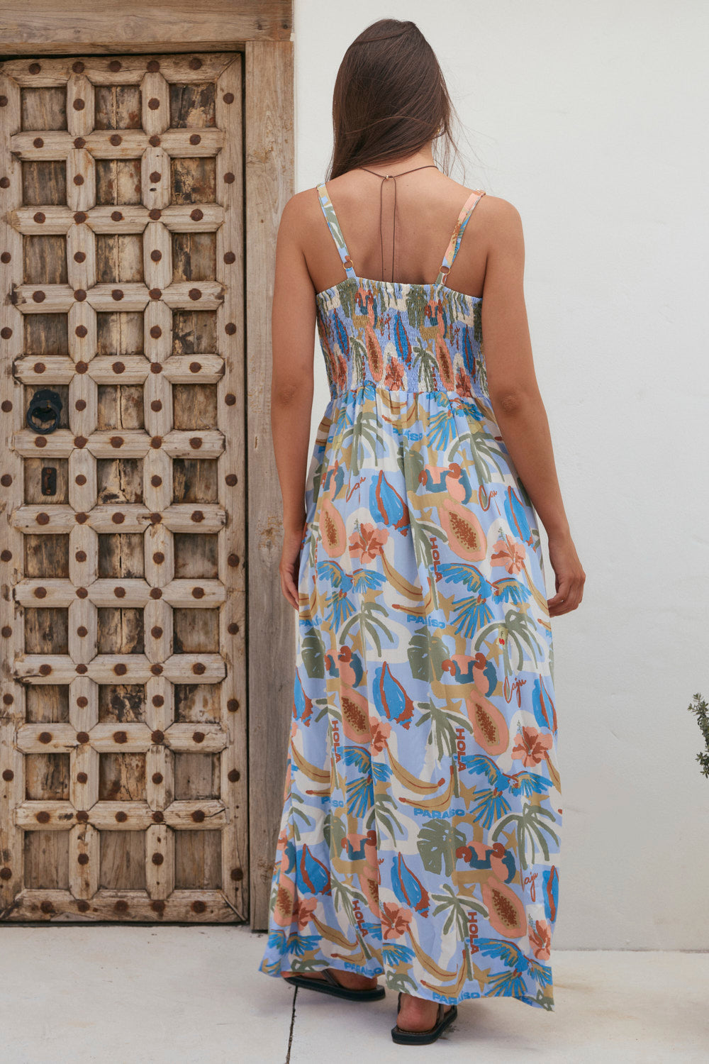 Woman wearing a floral dress standing in front of a wooden door.